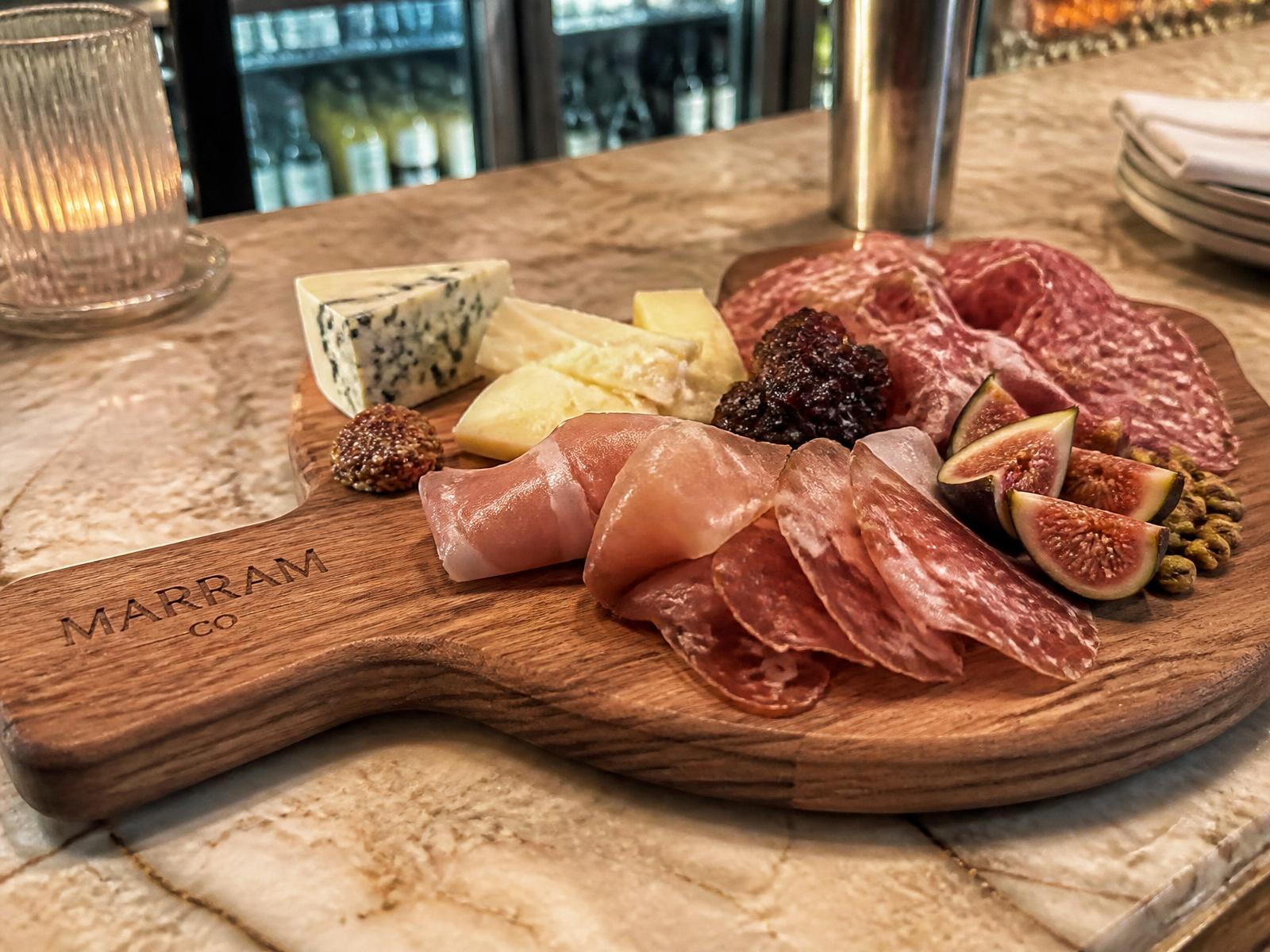 Logo-engraved custom cutting board used as a charcuterie serving board on a restaurant bar