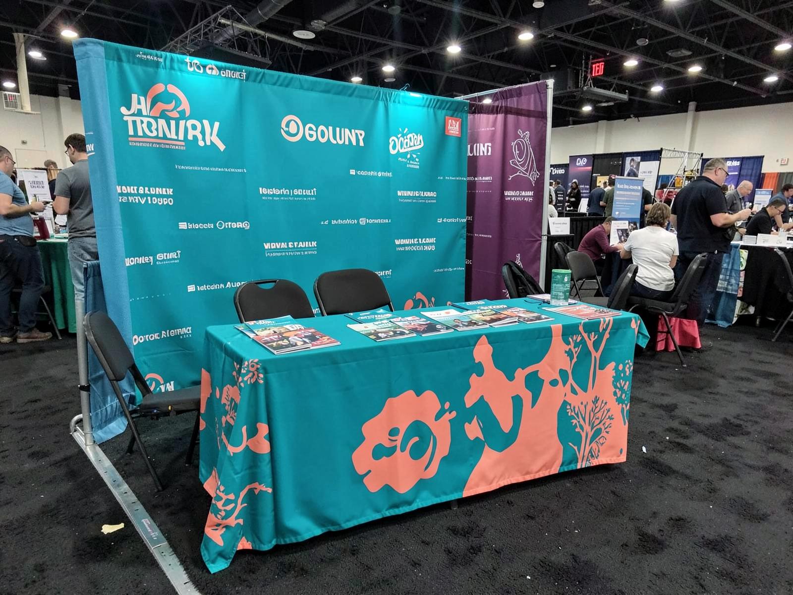 Trade show booth table with a full-color printed custom table cloth in teal and coral