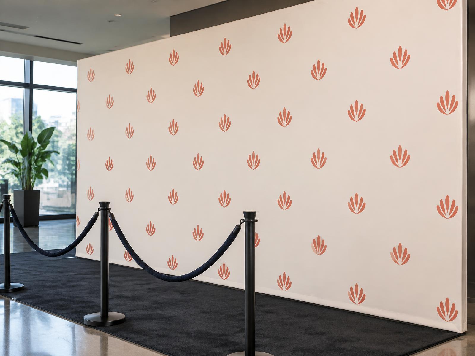 Step-and-repeat backdrop with a repeating coral logo pattern behind a press-line photo area