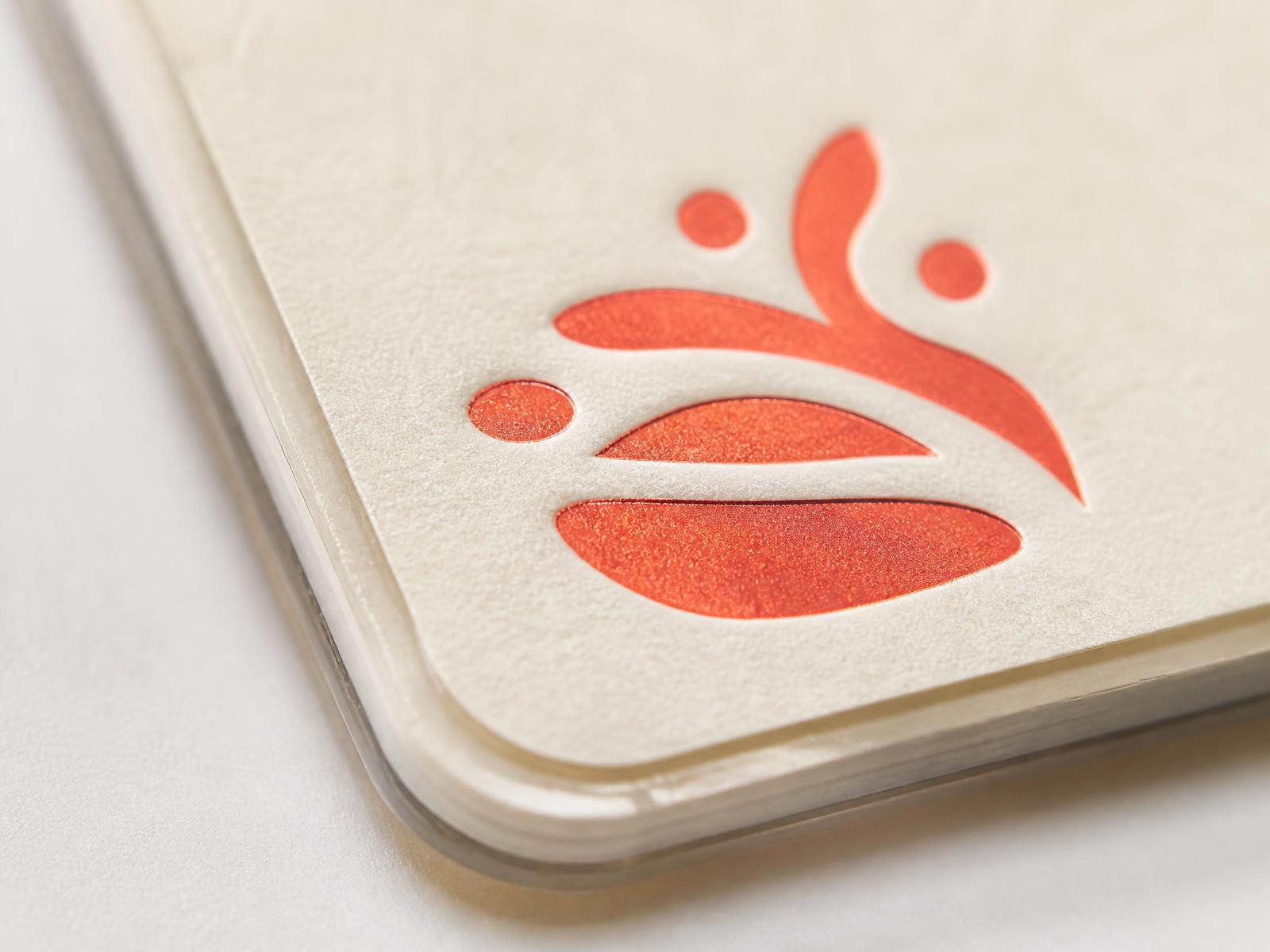 Macro close-up of a laminated cream custom bookmark edge with a crisp foil-stamped coral logo