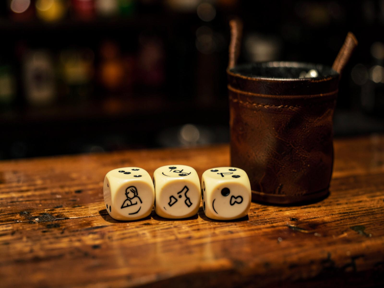 Cream logo-printed dice scattered beside a beer glass on a dark walnut bar top