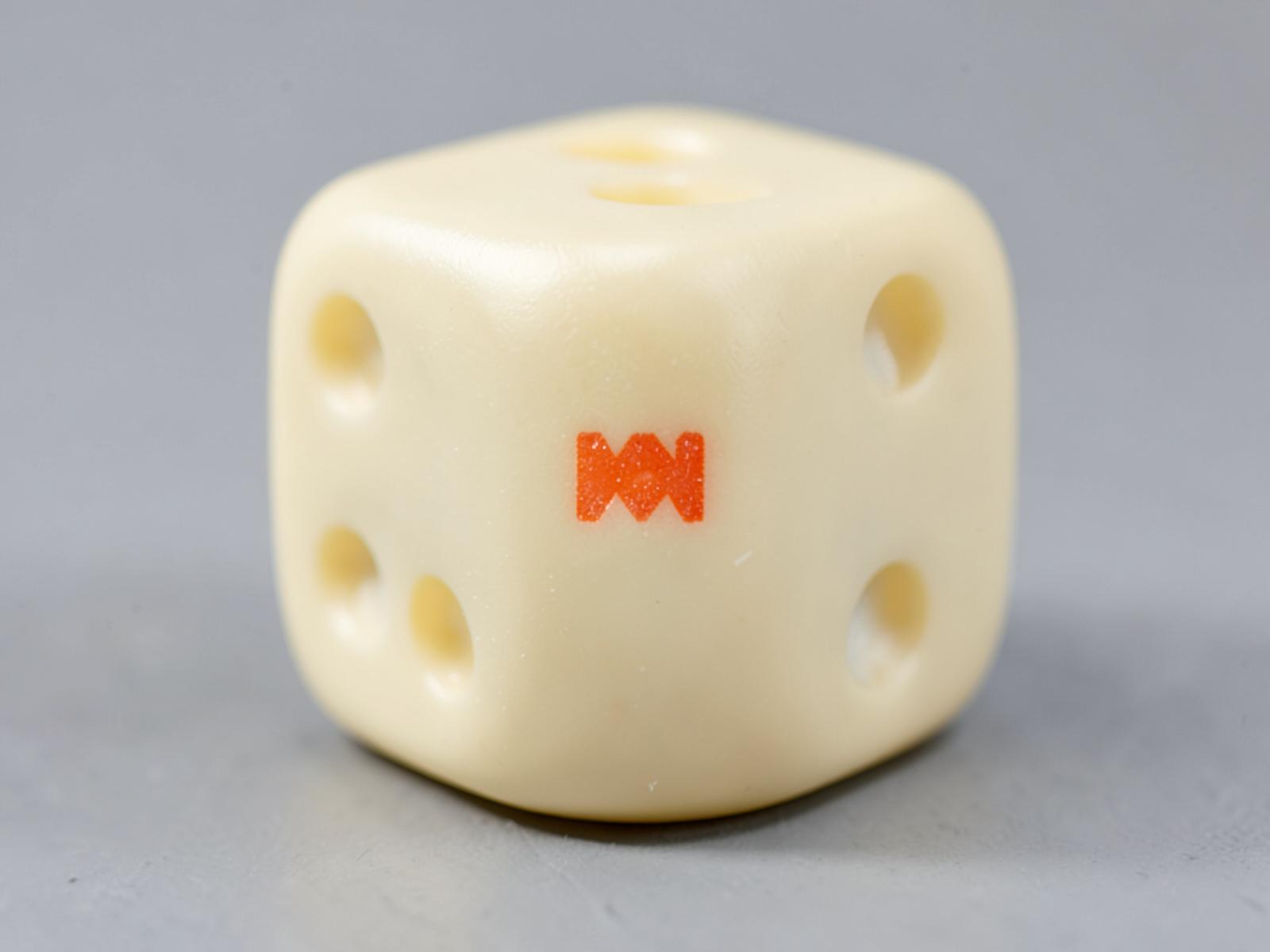 Macro close-up of a cream acrylic die with crisp coral printed pips and an engraved mark on one face