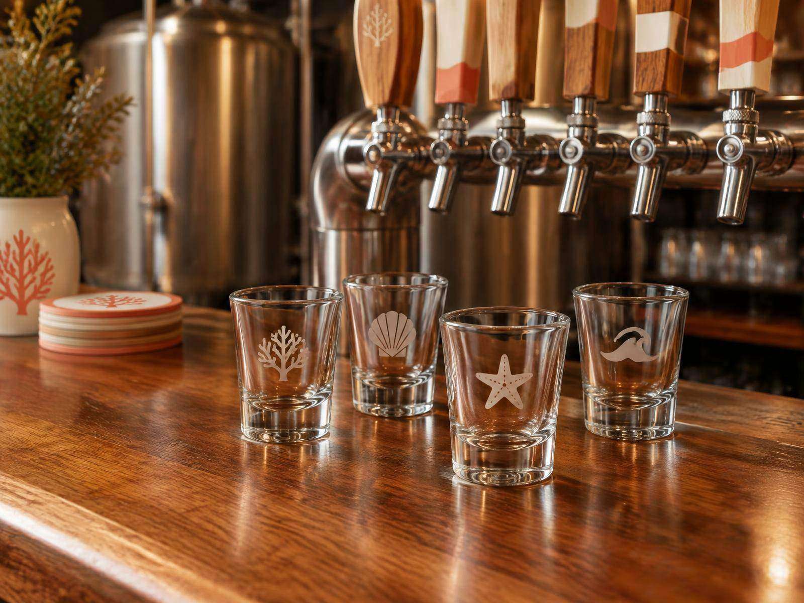 Custom logo-etched shot glasses on a brewery bar beside tap handles