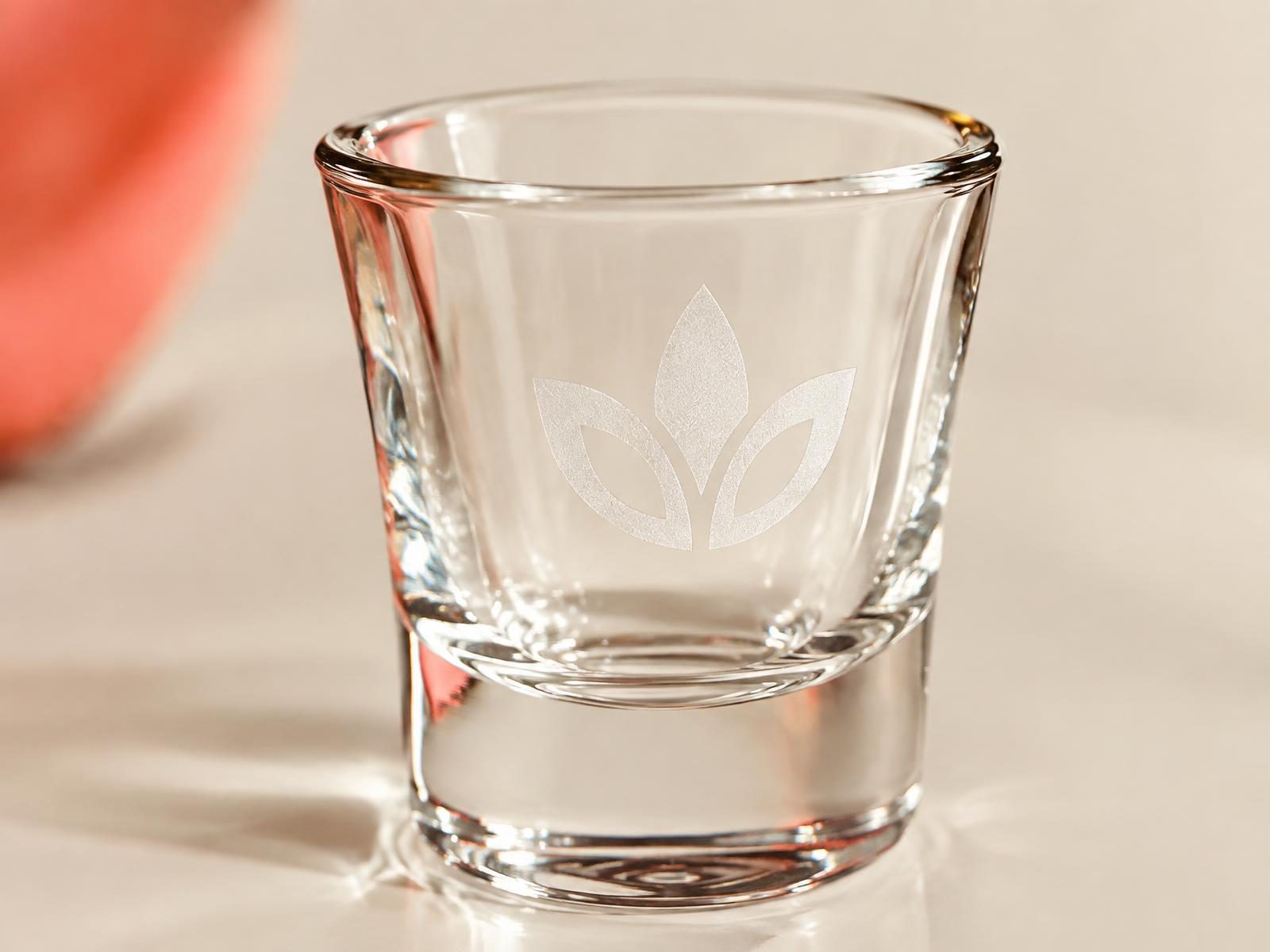 Macro close-up of a glass shot glass with a crisp laser-etched logo